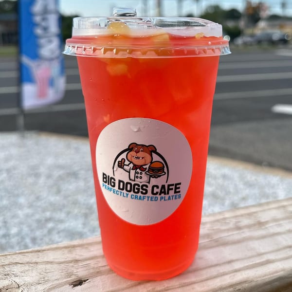 A Big Dogs Cafe branded cup filled with a red drink and fruit, resting on a wooden surface.