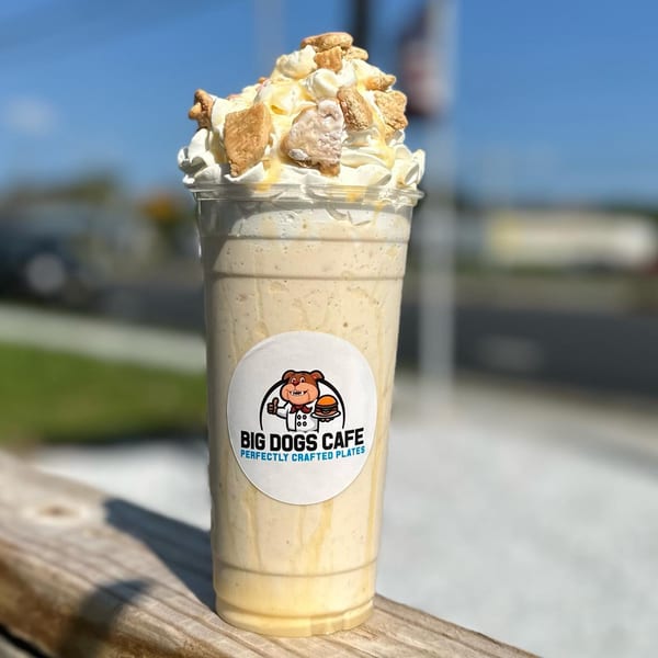 Big Dogs Cafe milkshake with whipped cream, caramel drizzle, and cookie pieces on a wooden railing.