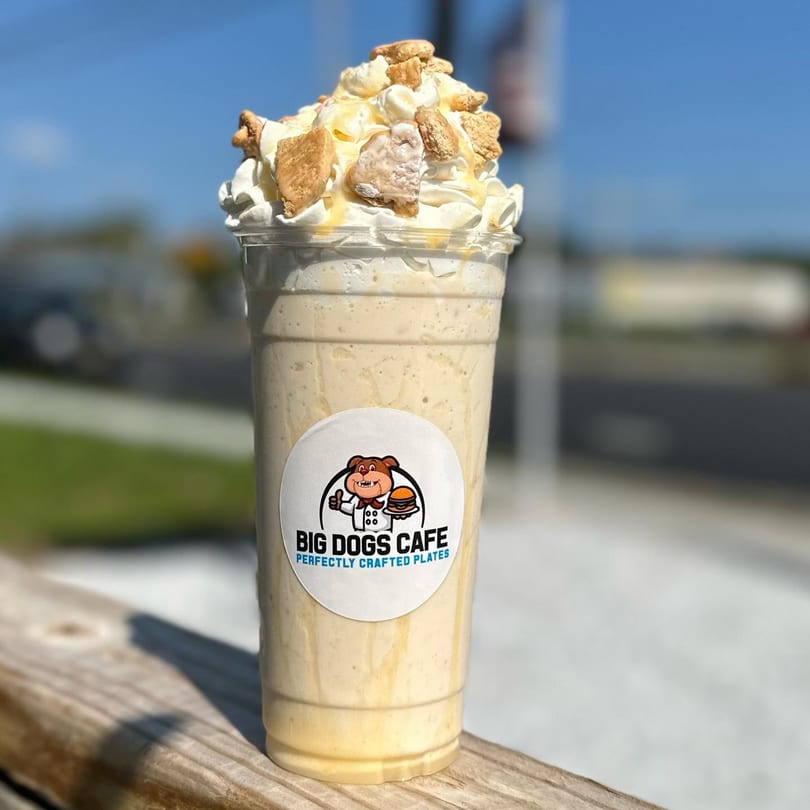 Big Dogs Cafe milkshake with whipped cream, caramel drizzle, and cookie pieces on a wooden railing.