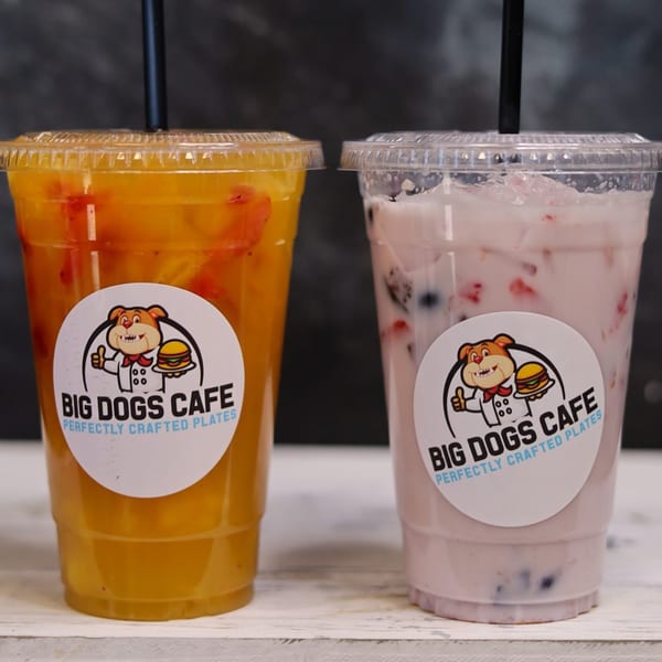 Two Big Dogs Cafe drinks, one orange and one pink, with black straws on a white surface.