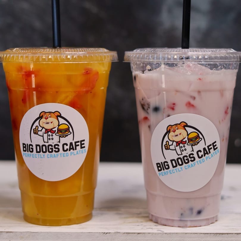 Two Big Dogs Cafe drinks, one orange and one pink, with black straws on a white surface.