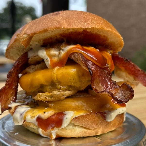 Big Dogs' burger with two patties, melted cheese, bacon, onion rings, and sauces on a bun.