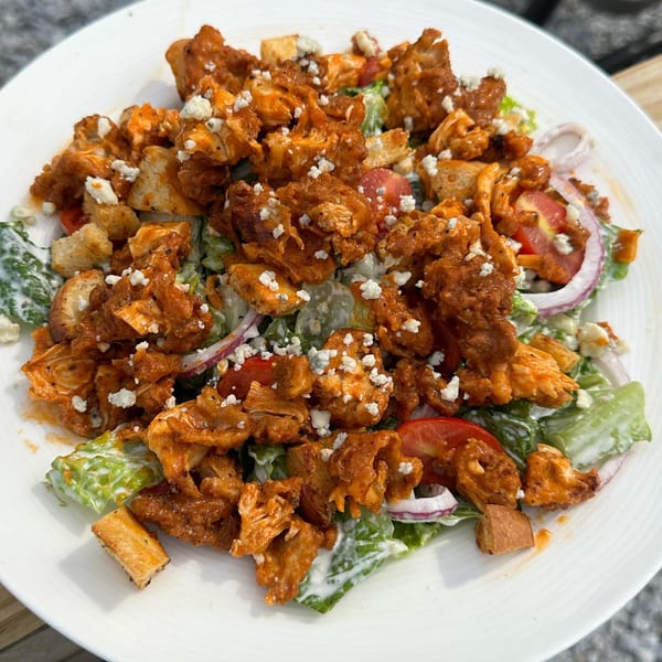 A buffalo chicken salad with blue cheese crumbles, tomatoes, red onion, and croutons.