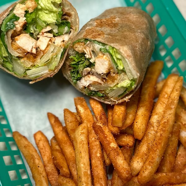 Two halves of a chicken Caesar wrap with lettuce and fries in a green basket.